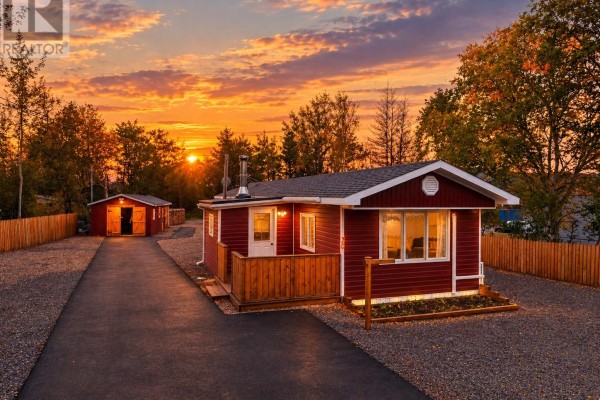 Red mobile home with white trim, wooden deck, and attached garage, silhouetted against a vibrant sunset sky. - 30 Ryder's Brook Road, Georges Brook