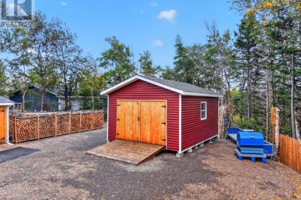 Small red detached garage with double wooden doors and a ramp, next to stacked firewood and outdoor seating. - 30 Ryder's Brook Road, Georges Brook