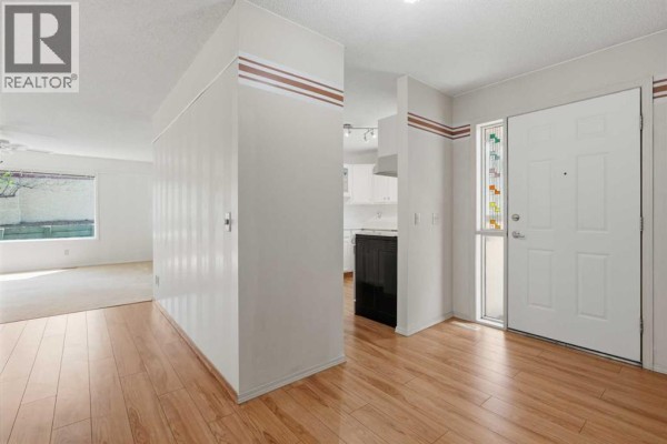 Interior hallway with wood-look flooring, beige walls, and a view into the living area and kitchen. - 30 Sandarac Circle Nw, Calgary
