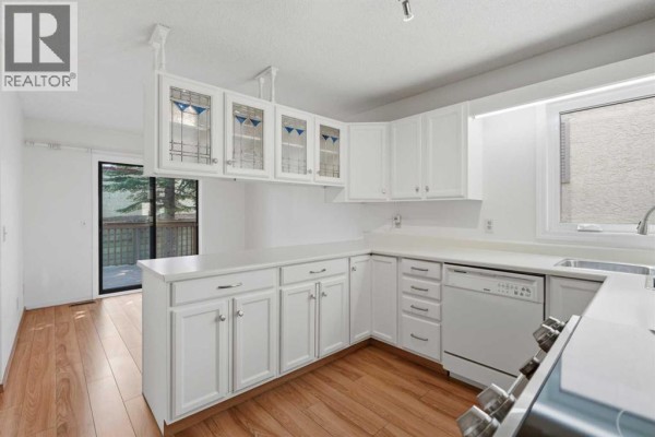 White kitchen with white cabinets, stainless steel appliances, and a breakfast bar with stained glass accents. - 30 Sandarac Circle Nw, Calgary