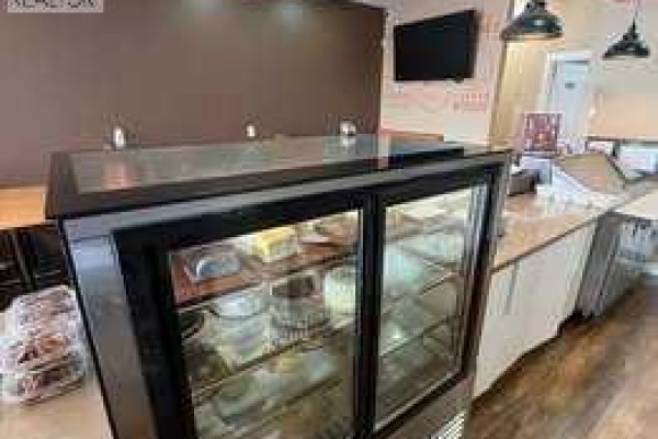 Commercial kitchen counter with display case, coffee machines, and large windows with natural light. - 30 Savanna Crescent Ne, Calgary