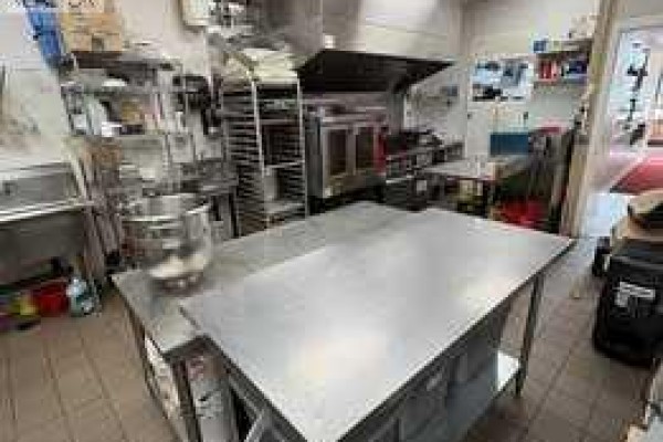 Stainless steel work tables and commercial baking ovens in a spacious commercial kitchen. - 30 Savanna Crescent Ne, Calgary