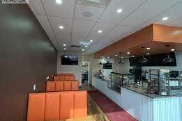 Interior view of a commercial space with a counter, display cases, and orange seating. - 30 Savanna Crescent Ne, Calgary