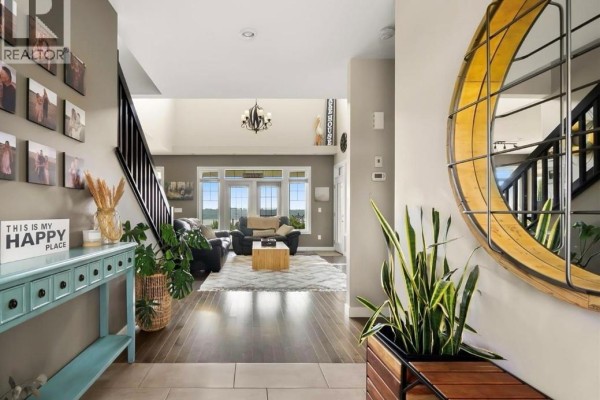 View from foyer into living room with dark wood floors, staircase, and large windows. - 30 Shore Acres Drive, Last Mountain Lake