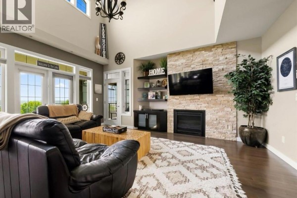 Living room featuring a stone fireplace, leather sofas, large windows, and high ceilings. - 30 Shore Acres Drive, Last Mountain Lake