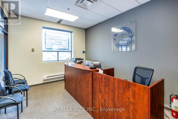 A reception desk with a computer and chairs in a waiting area with a window and a clear sign. - 300 - 274 Mackenzie Avenue, Ajax