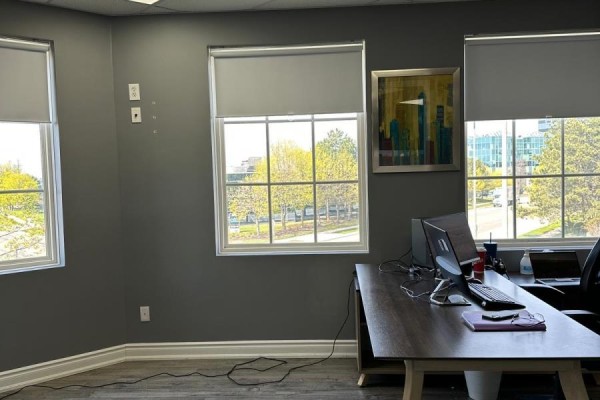 Office desk with computers and chairs next to three large windows with blinds. - 300 - 5045 Orbitor Drive, Mississauga
