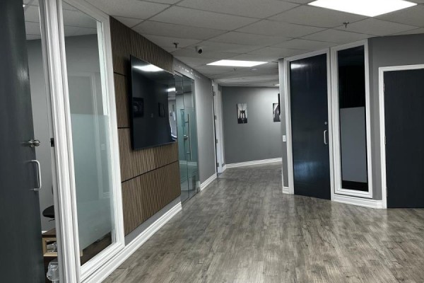 Modern office hallway with glass doors, wooden accent wall, and dark gray doors. - 300 - 5045 Orbitor Drive, Mississauga