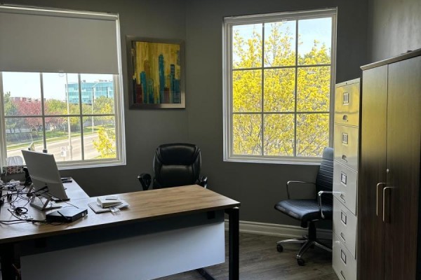 Office with a wooden desk, two chairs, filing cabinet, and large windows with trees. - 300 - 5045 Orbitor Drive, Mississauga
