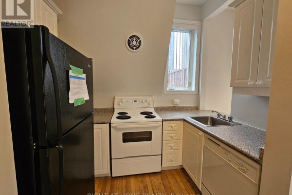 Compact kitchen with white cabinets, black refrigerator, white stove, and speckled countertops. - 300 - 524 Yonge Street, Toronto