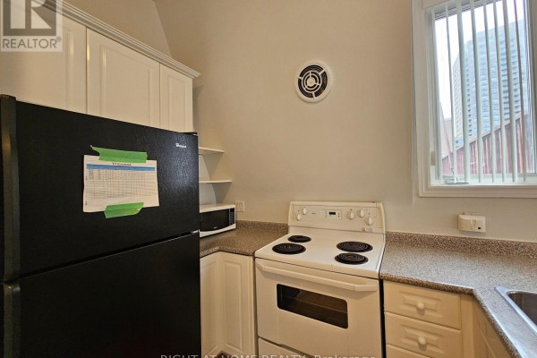 Kitchen view showing white cabinets, stove, sink, dishwasher, and a window overlooking a building. - 300 - 524 Yonge Street, Toronto