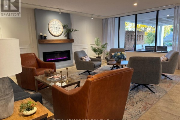 Apartment building lounge with fireplace, seating area, and large window with outdoor view. - 300 - 8 Fead Street, Orangeville