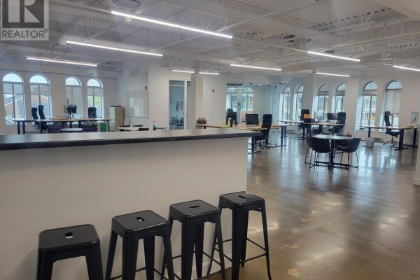 Open-plan office space with desks, chairs, and tables, featuring arched windows and polished concrete floors. - 300 - 80 Queen Street, Kingston