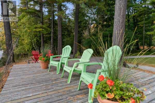 Light green Adirondack chairs arranged on a weathered wooden deck with potted plants and orange flowers. - 300 & 302 Isobel Lane, Tay Valley
