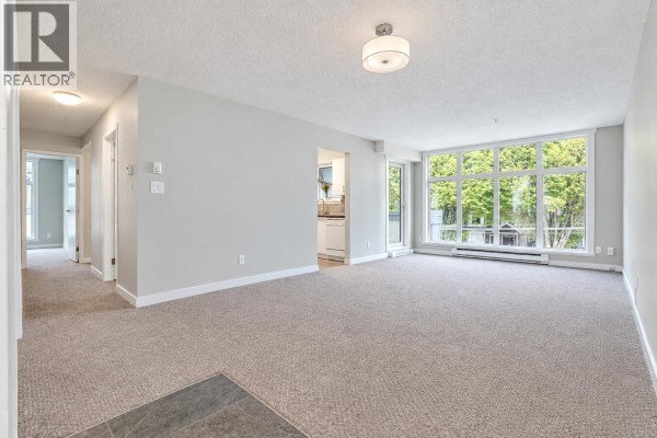 Empty living room with view to hallway and kitchen, and large windows. - 300 2533 Penticton Street, Vancouver