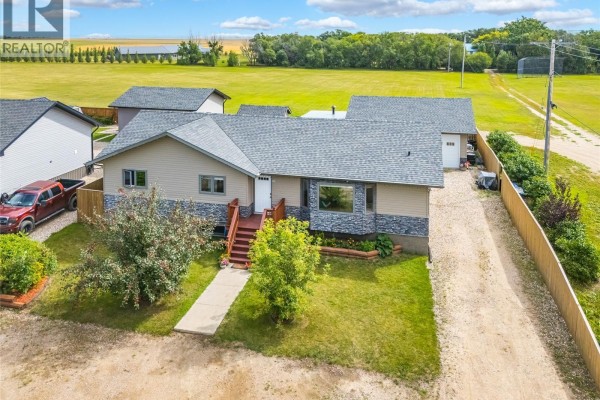 Exterior view of the beige house with attached garage and driveway on a dirt road. - 300 7th Street, Vonda