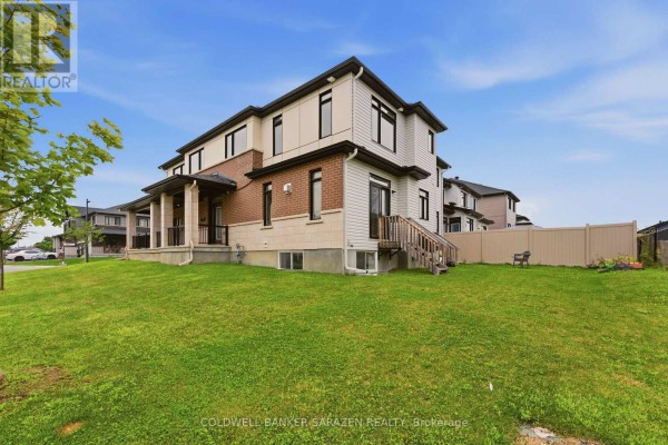 Rear exterior of a townhouse showing white siding, brick accents, and a grassy backyard. - 300 Ibanez Walk, Ottawa