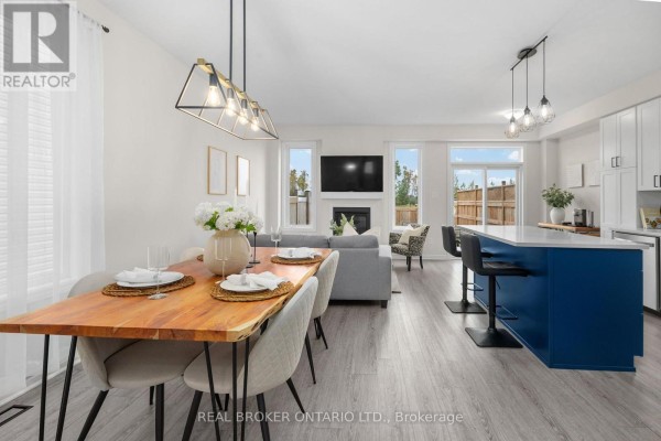 Open concept dining and living area with wooden dining table, grey sofa, fireplace, and kitchen island. - 300 Livery Street, Ottawa