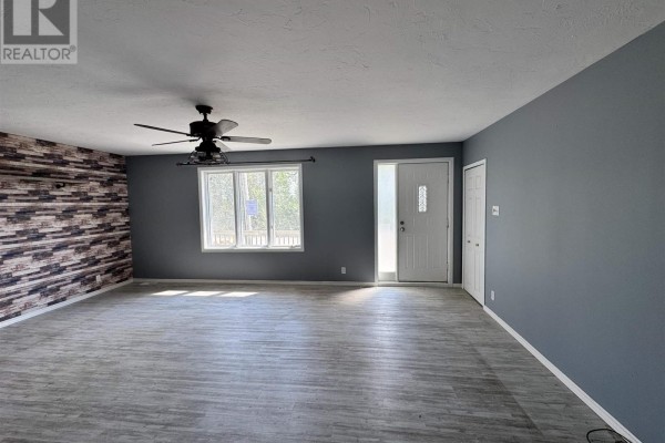 Another view of the spacious living room, showing the front door and a large window. - 300 Martel Rd, Chapleau