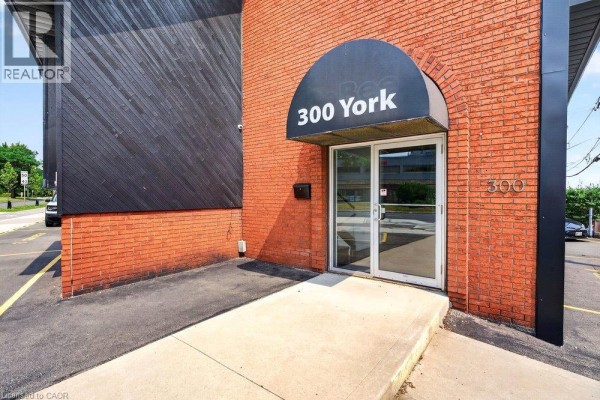 Entrance to 300 York building with a black arched awning over glass double doors and a concrete ramp. - 300 York Boulevard, Hamilton