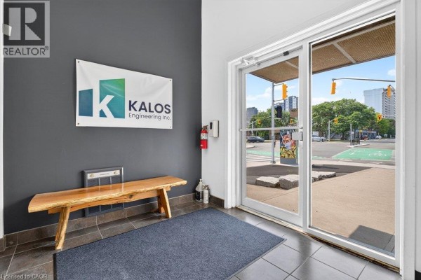 Building interior entrance area with gray walls, a wooden bench, dark tile floor, and a Kalos Engineering sign. - 300 York Boulevard, Hamilton