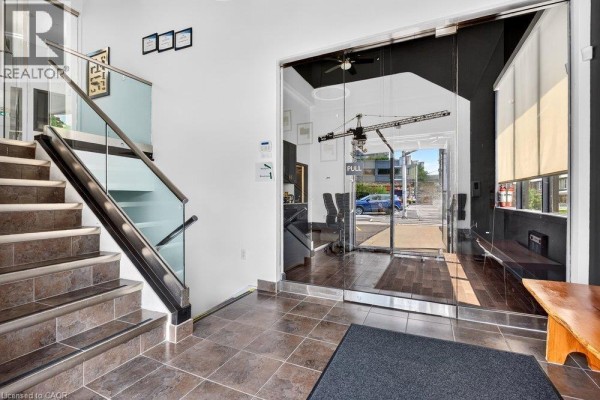 Interior view of a staircase with glass railings and a reception area with glass walls, viewed from the entrance. - 300 York Boulevard, Hamilton