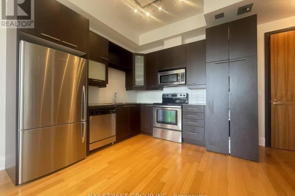 Kitchen with stainless steel appliances, dark wood cabinets, and hardwood floors. - 3001 - 500 Sherbourne Street, Toronto