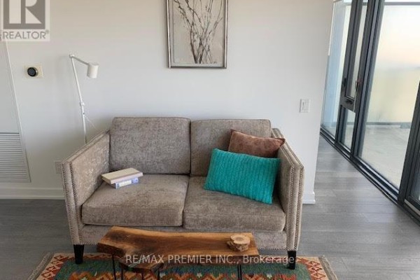 A beige sofa with decorative pillows sits on a rug in a living room space. - 3002 - 185 Roehampton Avenue, Toronto