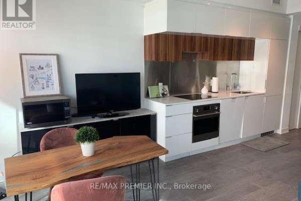 Compact kitchen with white cabinetry, stainless steel appliances, and a dining area. - 3002 - 185 Roehampton Avenue, Toronto