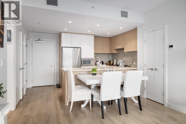 Dining area with white table and chairs, adjacent to the kitchen with light wood cabinetry. - 3002 567 Clarke Road, Coquitlam