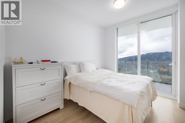 Bright bedroom with a double bed, white furniture, and large windows providing mountain views. - 3002 567 Clarke Road, Coquitlam