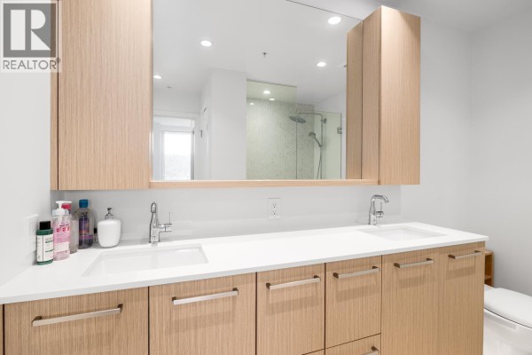 Bathroom with dual sinks, light wood cabinetry, and a glass shower enclosure. - 3002 567 Clarke Road, Coquitlam