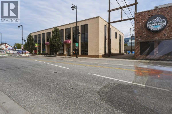 Rear parking lot with multiple cars parked in front of a beige commercial building with large windows. - 3003 30 Street, Vernon