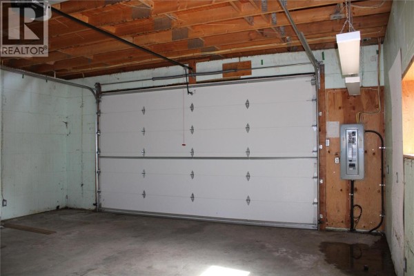 Interior view of a garage with two white overhead doors, concrete floor, and wood-paneled walls. - 3003 Squilax-anglemont Road, Lee Creek