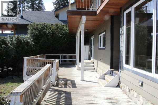 Wooden deck with white railings attached to a tan house with large windows. - 3003 Squilax-anglemont Road, Lee Creek