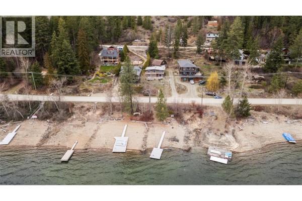 Overhead drone shot of houses and docks on a shoreline next to a wooded hillside. - 3003 Squilax-anglemont Road, Lee Creek