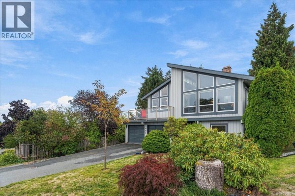 Side view of a gray house with a sloped roof, large windows, and mature landscaping including trees and shrubs. - 3005 Persimmon Pl, Nanaimo