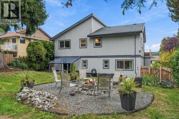 Backyard patio with a gravel base, fire pit, seating, and surrounding green grass and foliage. - 3005 Persimmon Pl, Nanaimo