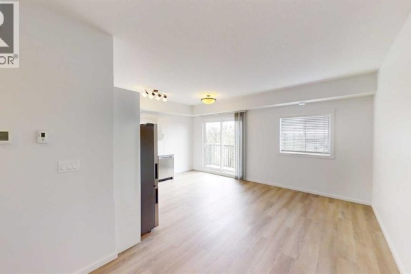Living room with light wood-look flooring, white walls, stainless steel refrigerator, and large windows. - 301, 10101 105 Avenue, Grande Prairie