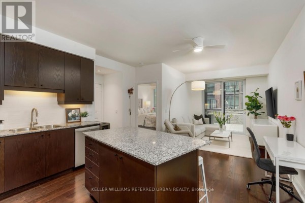 Open concept living area with dark wood cabinets, granite island, sofa, and desk. - 301 - 1 Scott Street, Toronto