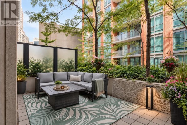 Outdoor patio furnished with a grey sectional sofa, coffee table, and green leaf patterned rug. - 301 - 1 Scott Street, Toronto