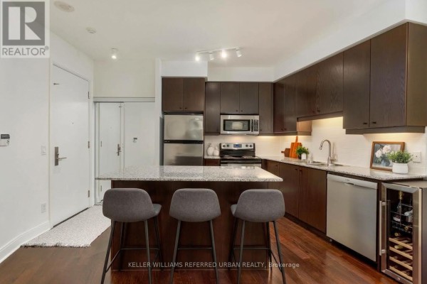 Kitchen with dark wood cabinetry, stainless steel appliances, granite island, and wine fridge. - 301 - 1 Scott Street, Toronto