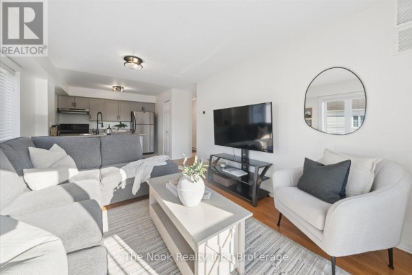 Living room with grey sectional sofa, white armchair, television, and view of kitchen. - 301 - 106 Aspen Springs Drive, Clarington