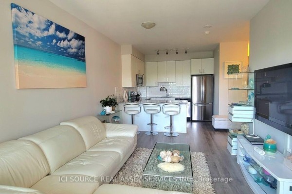 Living room with white leather sofa, kitchen island, bar stools, and wall-mounted TV - 301 - 11611 Yonge Street Richmond Hill