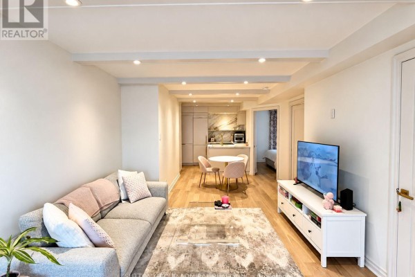 Living room with grey sofa, patterned rug, and television, opening to dining area and kitchen. - 301 - 1174 Yonge Street, Toronto
