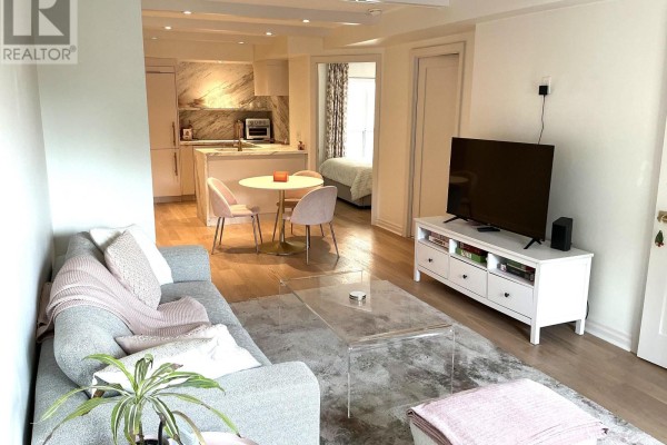 Living room featuring a sofa, coffee table, and television, with views into the dining area and kitchen. - 301 - 1174 Yonge Street, Toronto