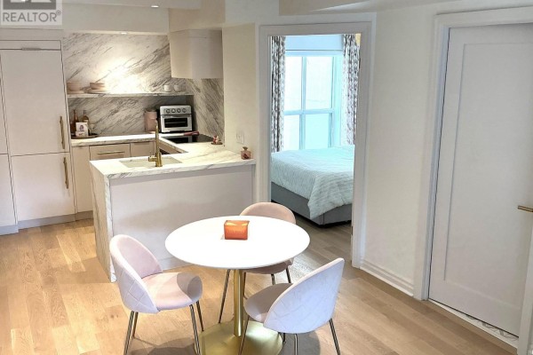 Compact kitchen with marble backsplash and light wood floors, next to a small dining table and a bedroom. - 301 - 1174 Yonge Street, Toronto