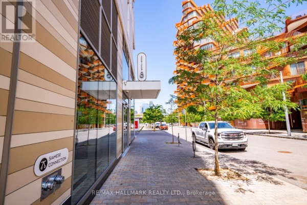 Street view of building facade with glass windows and trees. - 301 - 118 Merchants' Wharf, Toronto
