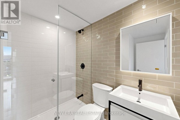 A bathroom with white marble tile walls, a white bathtub, toilet, and a modern white vanity with a silver faucet. - 301 - 150 Logan Avenue, Toronto