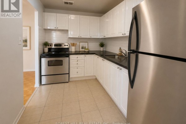 L-shaped kitchen with white cabinets, black countertops, stainless steel appliances, and tile flooring. - 301 - 165 Kennedy Road, Brampton